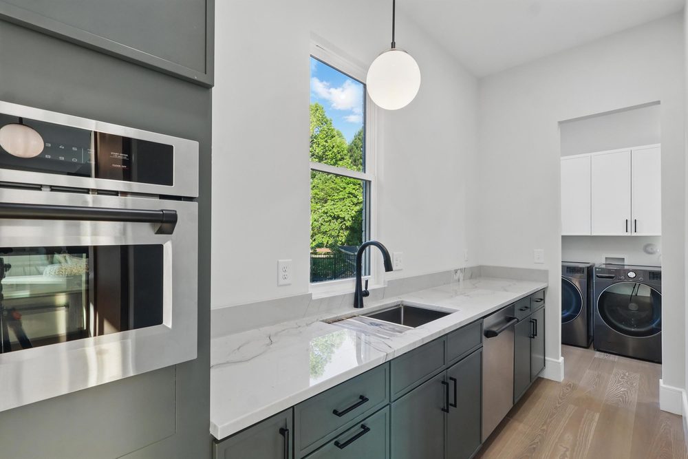 Sage green butler's pantry cabinets with a quartz counter and undermount sink, opening into a white laundry room