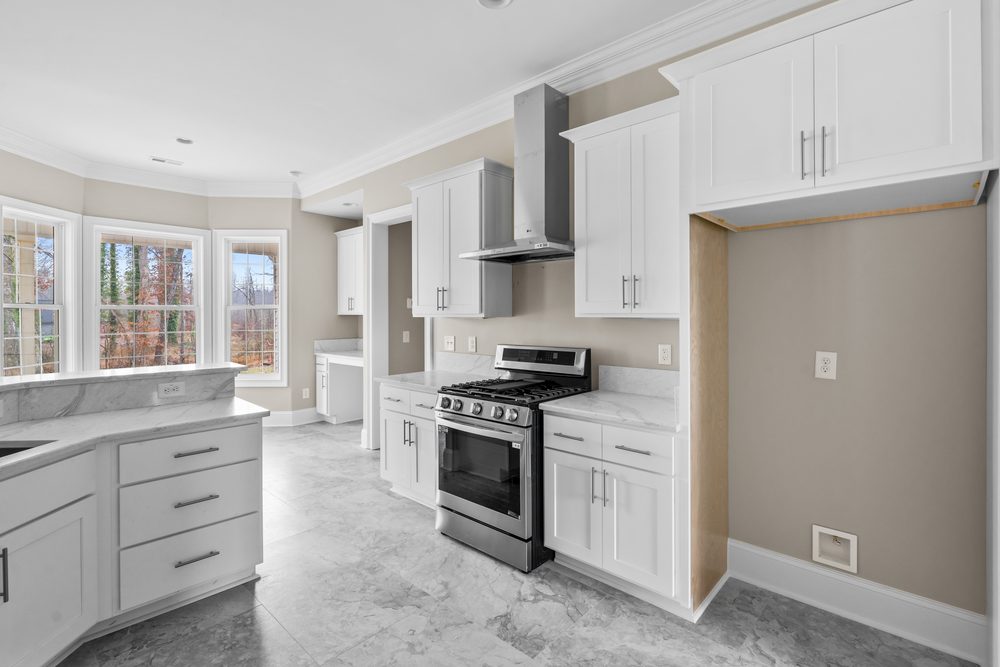 White shaker galley kitchen with a stainless range, chimney hood and cased refrigerator opening