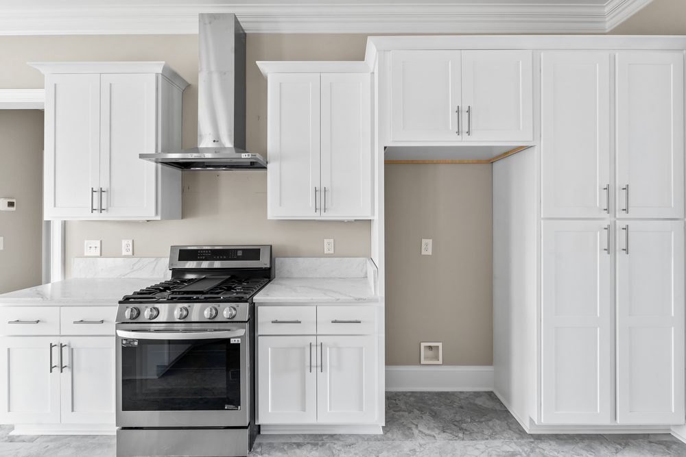 White shaker range wall with a stainless chimney hood and a tall 96-inch pantry cabinet